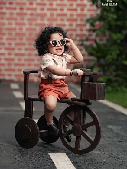 A stylish little boy with sunglasses, enjoying a ride on his wooden tricycle.
