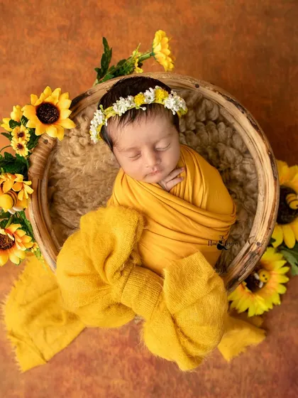 A beautiful swaddled newborn surrounded by sunflowers in a rustic basket. Swaddling helps keep babies feeling secure and allows for these peaceful, womb like poses.