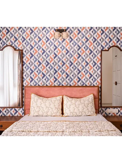 A full view of the bed in the geometric-wallpapered room, showing the two arched mirrors that flank the peach headboard.
