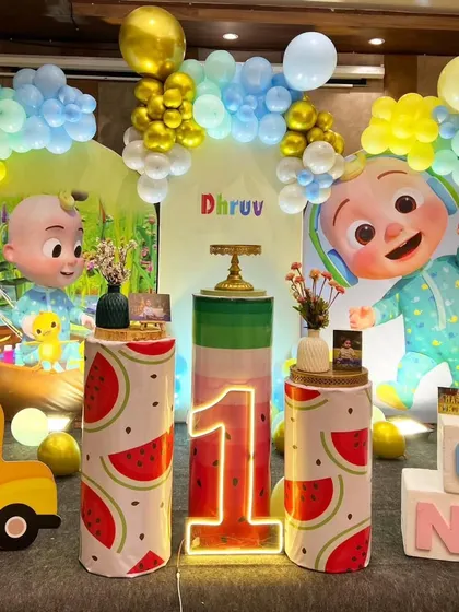 A grand Cocomelon first birthday with themed pedestals. This setup includes a large backdrop, character cutouts, and a light-up number '1' with 'ONE' blocks.
