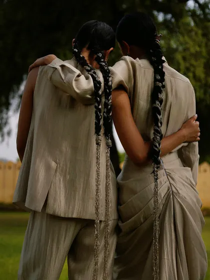 A tender moment between two models, showcasing the back of their outfits and their matching braided hairstyles.