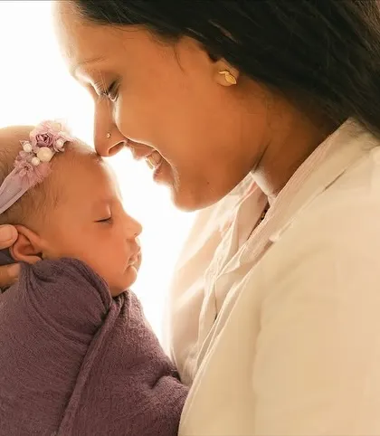 A close-up of a mother and her sleeping baby, forehead to forehead.