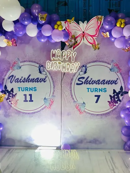 A shared birthday celebration with a purple and white Butterfly theme, featuring two personalized backdrops within one balloon arch.