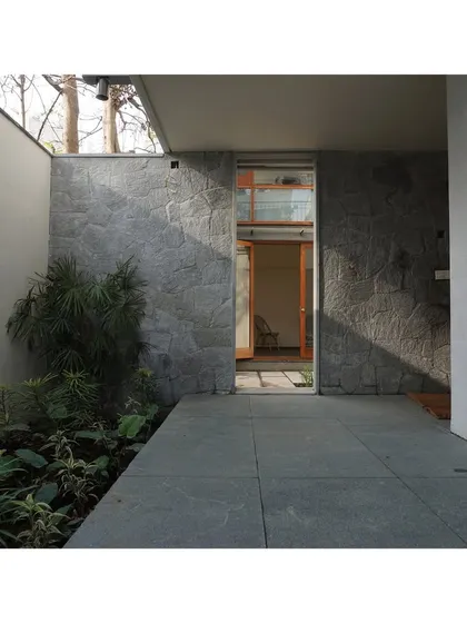 The entrance to the RT Nagar residence, where a textured stone wall guides visitors towards the door.