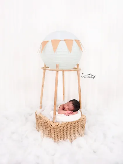 Another take on the hot air balloon theme, this shot captures the baby in a slightly different, curled-up pose. The consistent white background ensures a clean and timeless collection of images.