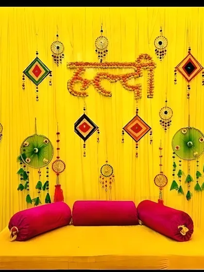 A traditional Haldi ceremony backdrop featuring a bright yellow fabric background with intricate dreamcatcher and tassel hangings. The seating is arranged for the ceremony, showing how I can cater to cultural and pre-wedding events with specific decor needs.