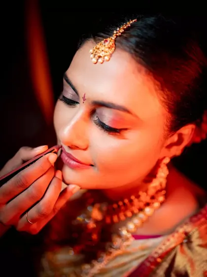 A close-up shot of a makeup artist applying lipstick to the bride, capturing the final details of her bridal look.
