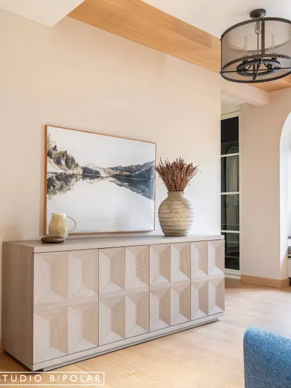 The master bedroom at Sunlit Serenity features a stunning carved wooden console table. The light wood and geometric pattern add visual interest and contrast with the room's soft, neutral tones.