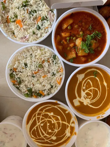 A close-up of some of the main courses from a large party order, including Veg Pulao, Aloo Mutter, and a creamy paneer gravy.