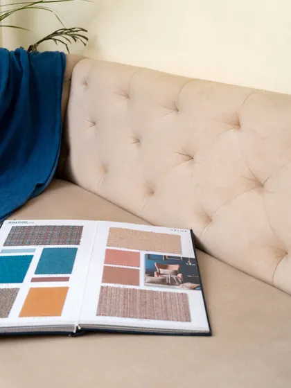 A detail shot of the tufted sofa, with a fabric swatch book resting on it, illustrating the process of selecting the perfect upholstery to match a client's vision.