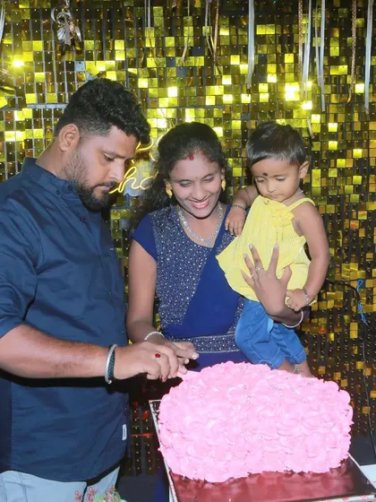 A happy family moment during a cake-cutting ceremony. The golden shimmer wall and purple balloons create a festive and photogenic background.