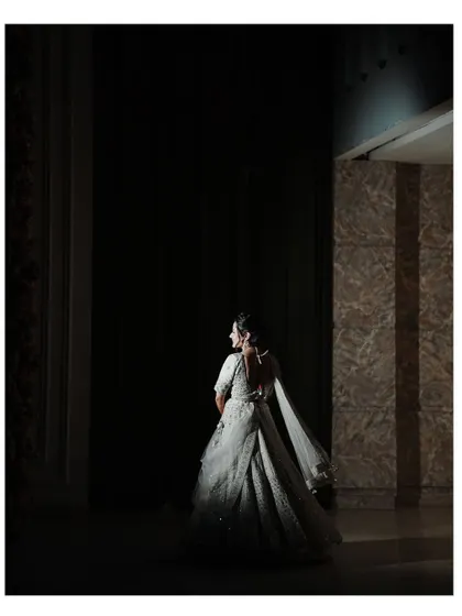 A dramatic, low-key portrait of the bride. The single light source highlights the silhouette of her gown, creating an artistic and mysterious image.