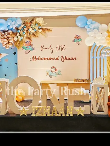 This 'Beary One' teddy bear theme for Mohammed Izhaan is incredibly sweet and charming. The setup on a stage features soft blue and beige tones, fluffy cloud-like balloons, and adorable teddy bears, creating a dreamy and gentle atmosphere.