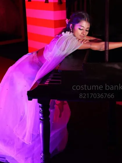 A model in a light blue gown posing with a piano prop under dramatic red lighting.