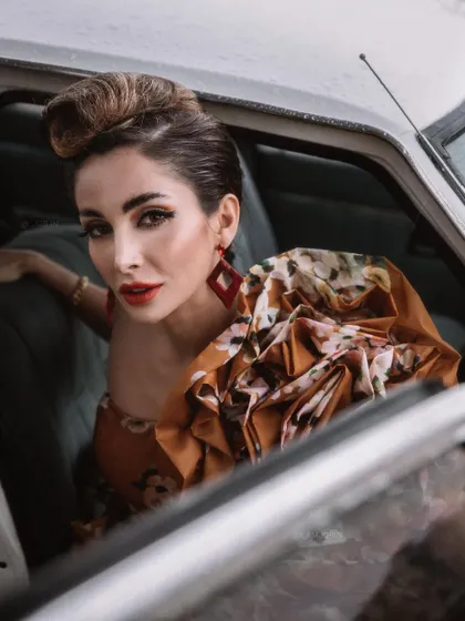 A close-up from the 'BLANCH' editorial, capturing the mood from inside the vintage car. The floral dress with its dramatic shoulder detail and the bold red lip are central to the glamorous, old-world narrative.