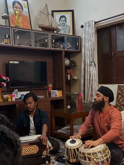 A wider view of the intimate baithak setting, performing for Pt. Mukund Bhale ji. The portraits of legendary musicians in the background add to the traditional atmosphere.