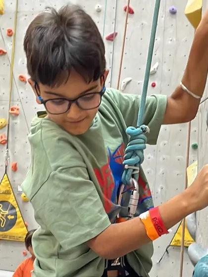 A young climber learns how to properly attach his belay device. Safety is our top priority, and we teach it from the very beginning.