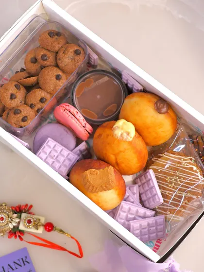 An unboxed view of our indulgent Rakhi Grazing Box, showing the variety of treats inside, including bombolinis, macarons, and cookie cereal with a dipping sauce.