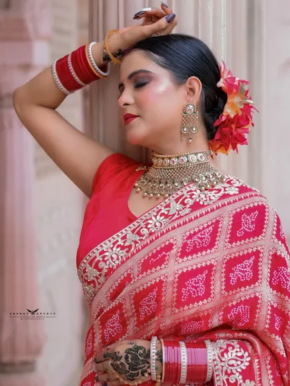 A serene close-up of a woman in a red saree, leaning against a pillar with her eyes closed. The flowers in her hair add a touch of natural beauty.