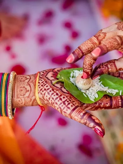 A detailed shot of a ritual during a South Indian wedding, where the bride's henna-adorned hands hold a betel leaf with rice and areca nut.
