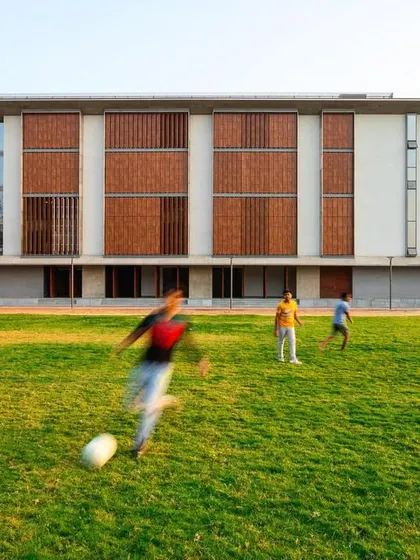 The grounds of the JSW School of Public Policy at IIM Ahmedabad provide ample space for recreation and relaxation. The building's facade, with its pattern of solid and void, serves as a backdrop to the active campus life.