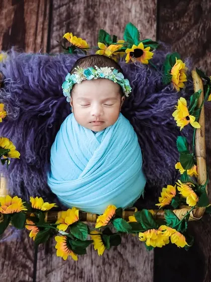 A baby swaddled in blue, framed by yellow flowers in a square basket, creating a colorful and cheerful composition.