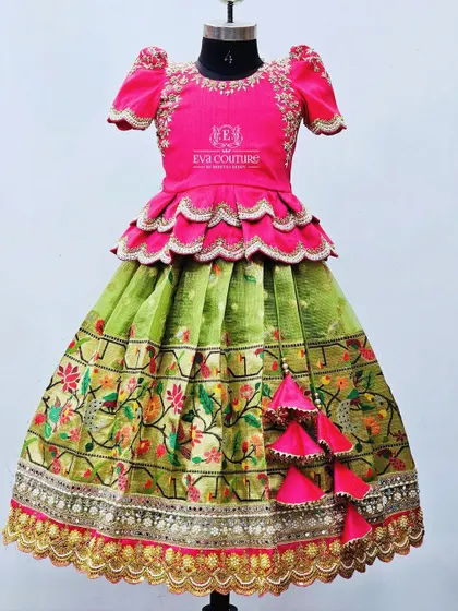 A grand designer lehenga in pink and green. The pink peplum top has scalloped edges, and the green skirt features a heavy Paithani-style embroidered border with an additional layer of gold work.
