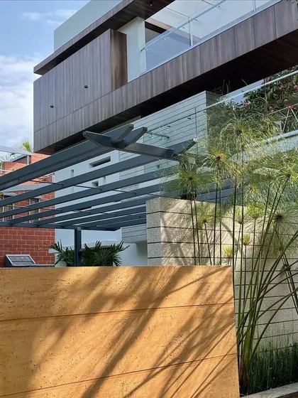 The shadow of a pergola falls across a stone-clad boundary wall, adding a layer of visual interest and texture to the entrance of the 'Hongirana' home.