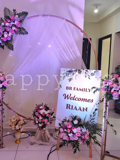 A personalized welcome sign for baby Riaan's naming ceremony. The modern circular arch is decorated with pink and white flowers and fairy lights, creating a warm welcome for guests.