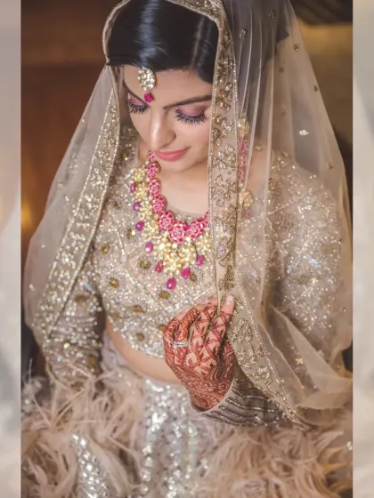 A close-up portrait of a bride looking down, her face partially covered by her delicate veil. The shot highlights her stunning jewelry and the intricate details of her outfit.