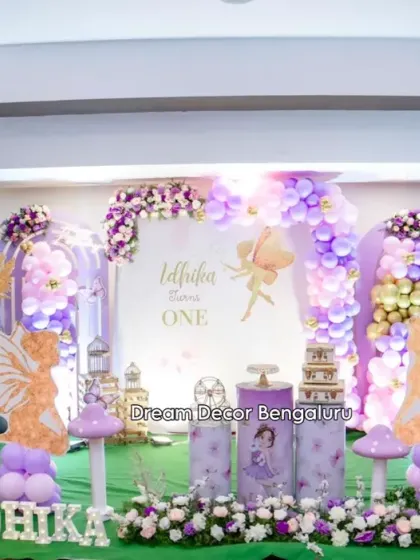 A beautiful butterfly-themed first birthday with a purple and gold color scheme. The setup includes fairy cutouts, mushroom props, and a lush green carpet.