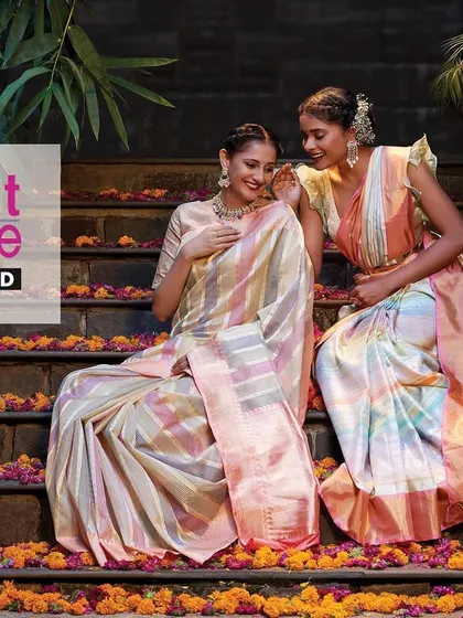 A campaign shot for Kasat Exclusive featuring their stunning sarees. The models are posed on stone steps adorned with flowers, creating a scene that is both traditional and contemporary.