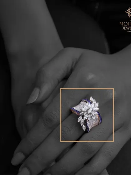 A modern, artistic ring with a butterfly or floral motif, crafted with marquise diamonds and sapphires. The black and white photo with a color pop emphasizes its unique design.