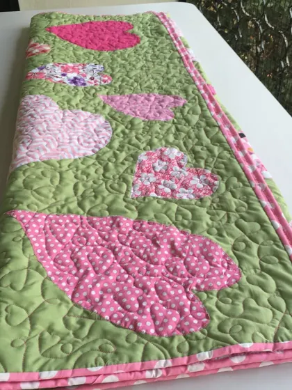 A sweet quilt with large, appliqué hearts in shades of pink on a green background.