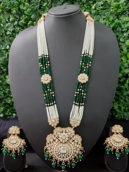 A magnificent long necklace set for rent, featuring a large kundan pendant and matching earrings. The green and white pearl beadwork adds a touch of royalty.