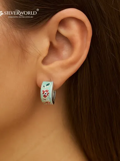 Our floral enamel hoop earrings are perfect for adding a pop of color. The delicate red and green floral pattern is hand-painted onto a silver base, creating a cheerful and stylish accessory.