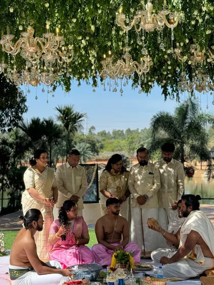 A beautiful moment from a Nischitartham ceremony, taking place under a canopy of lush greenery and dozens of hanging crystal chandeliers.