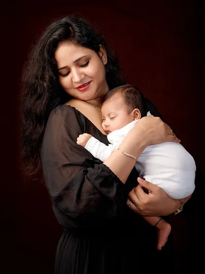 Cradled in love, a mother holds her sleeping newborn. This classic portrait against a dark backdrop is timeless, elegant, and full of maternal love.