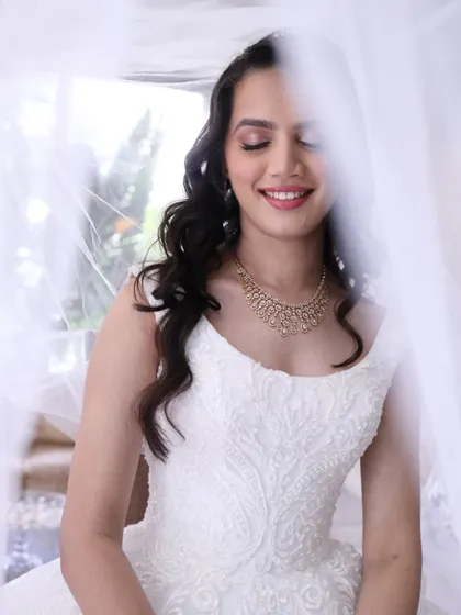 A serene moment captured under the veil. The soft lighting highlights the gentle shimmer on her eyes and the flawless finish of her makeup.