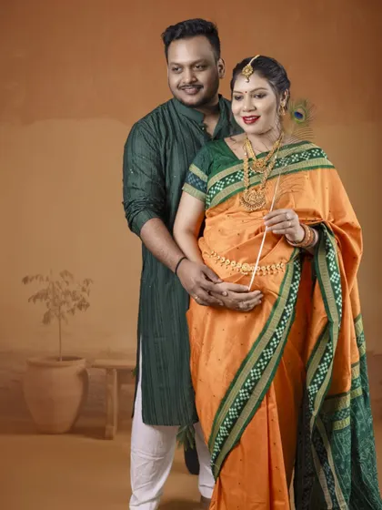 A classic standing portrait of the couple in traditional Indian attire. The simplicity of the pose highlights the beauty of the orange and green saree and their connection.