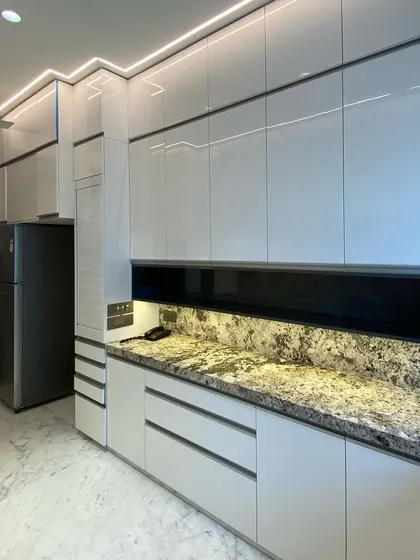 A full view of our acrylic kitchen at Lodha World Tower. The floor-to-ceiling white high-gloss cabinets create a sense of height and space, while the black glass backsplash adds a sleek, contrasting element.