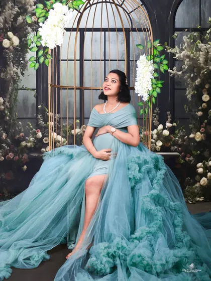 A stunning portrait in our golden birdcage prop, adorned with flowers. The mom-to-be's serene expression and the flowing teal gown create a truly magical image.