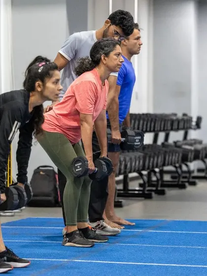 A group of runners performs dumbbell rows, focusing on building upper body and back strength to maintain good posture and form during long runs.