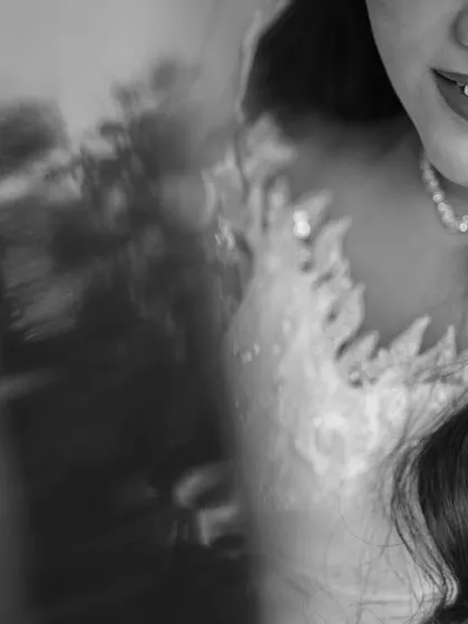 A close-up black and white shot of the bride's smile and the delicate lace of her wedding gown. This intimate detail shot captures her joy and the beauty of her bridal look.