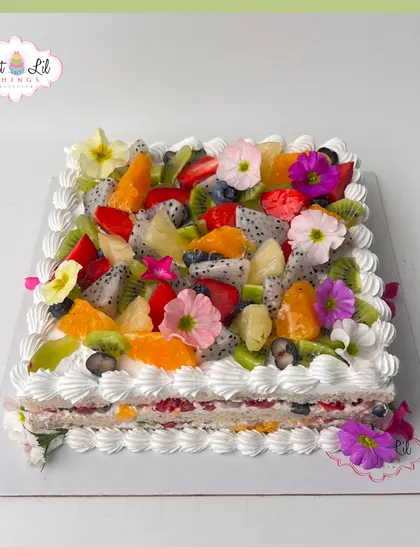 A refreshing and beautiful cake topped with a vibrant assortment of fresh fruits like strawberries, kiwi, and dragon fruit, along with edible flowers.