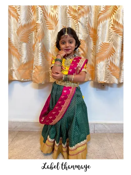Another photo of the little girl in her green, yellow, and pink lehenga set, looking absolutely adorable.