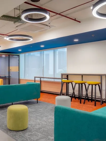 A vibrant and colorful lounge area with teal sofas, yellow bar stools, and a mix of textures. This space is designed to be an energetic hub for employees to connect and share ideas.