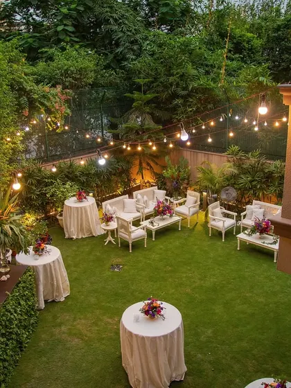 The same garden party setup, showing the beautiful ambiance created by the warm bistro lights as evening approaches. The space feels both elegant and inviting.