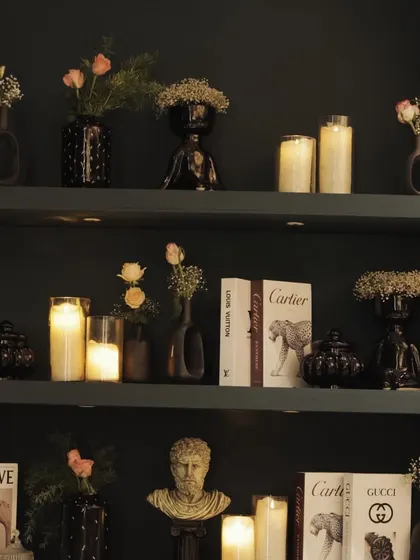 A sophisticated decor detail for a cocktail party, featuring a curated shelf with books, candles, and small floral arrangements.