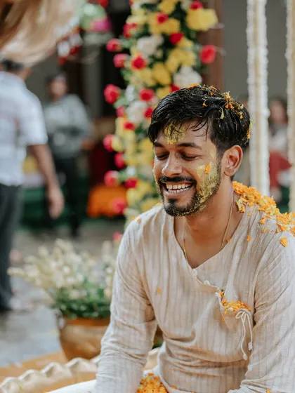 A happy, candid shot of the groom, his face smeared with turmeric, smiling brightly during his Haldi ceremony.